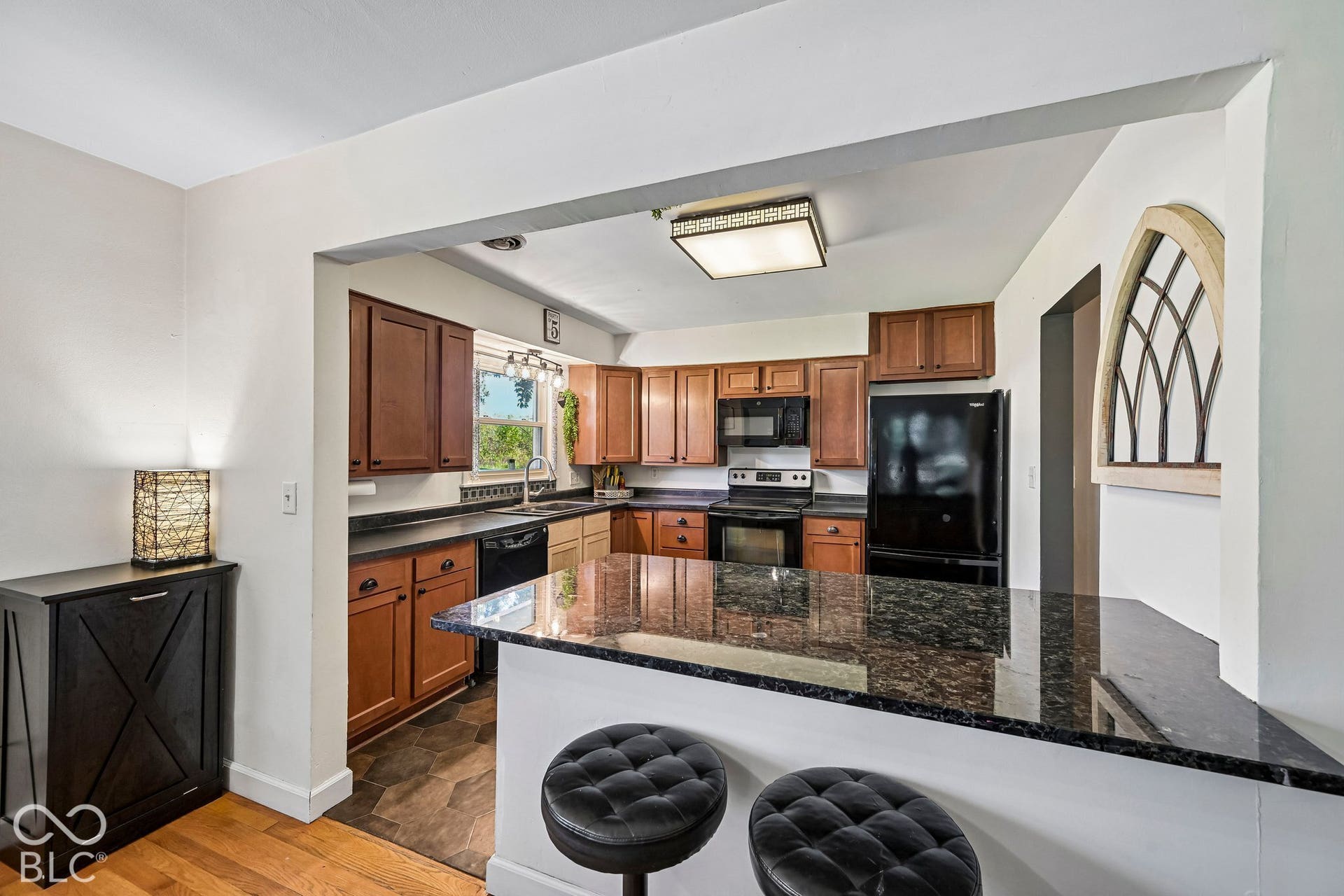 Kitchen featuring dark-finish cabinetry, black appliances, granite countertops, and a wood-finish floor