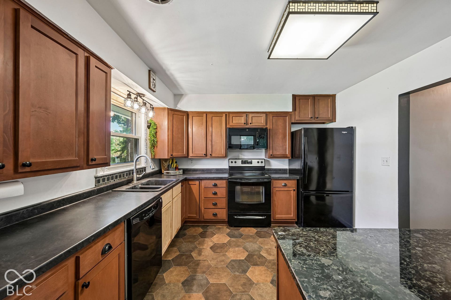 Kitchen featuring wood-finish cabinetry, black countertops, and a full suite of black appliances