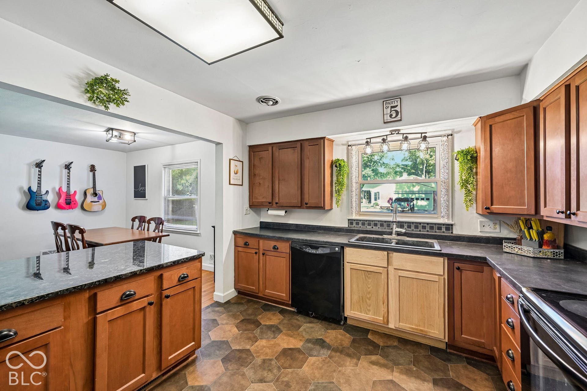 Kitchen featuring a dark granite-finish island, hexagonal tile flooring, wood cabinetry, built-in dishwasher, and a double basin sink