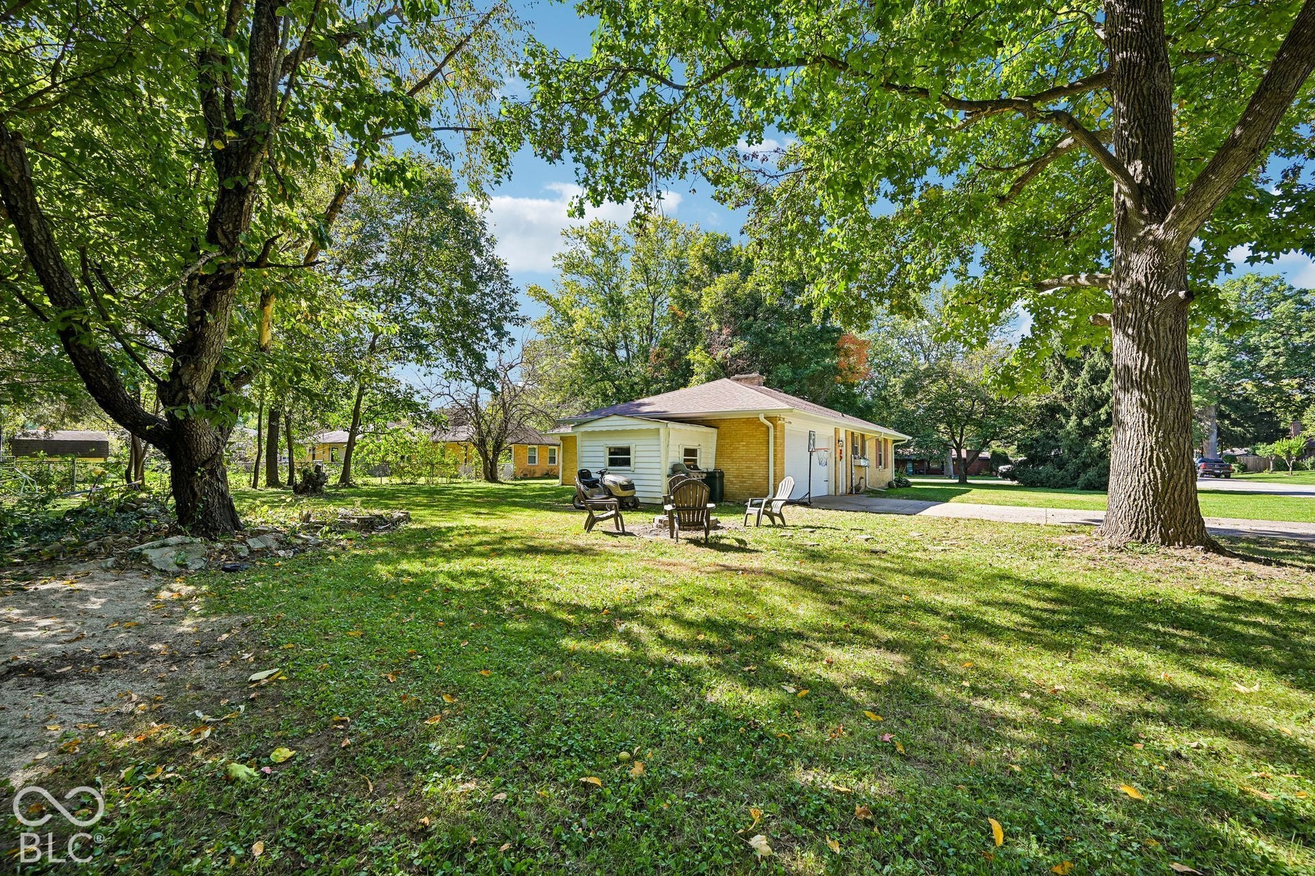 Expansive backyard with a manicured lawn, mature trees, and a gravel driveway