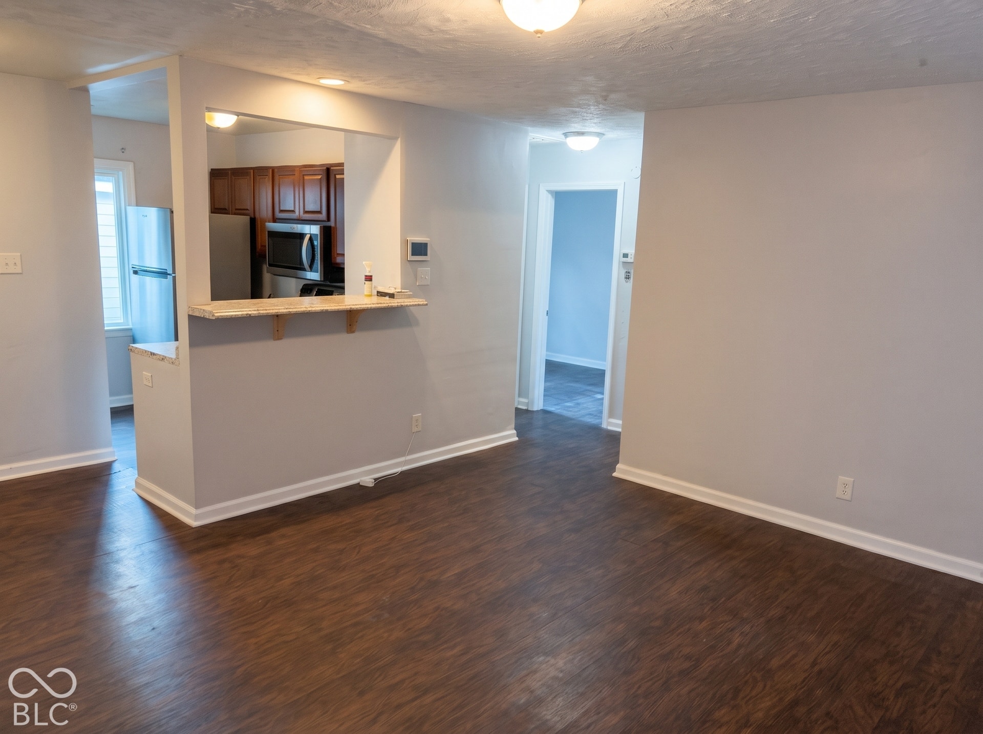 Wood-finish flooring, kitchen pass-through with breakfast bar, stainless steel refrigerator, stainless steel microwave, and recessed lighting
