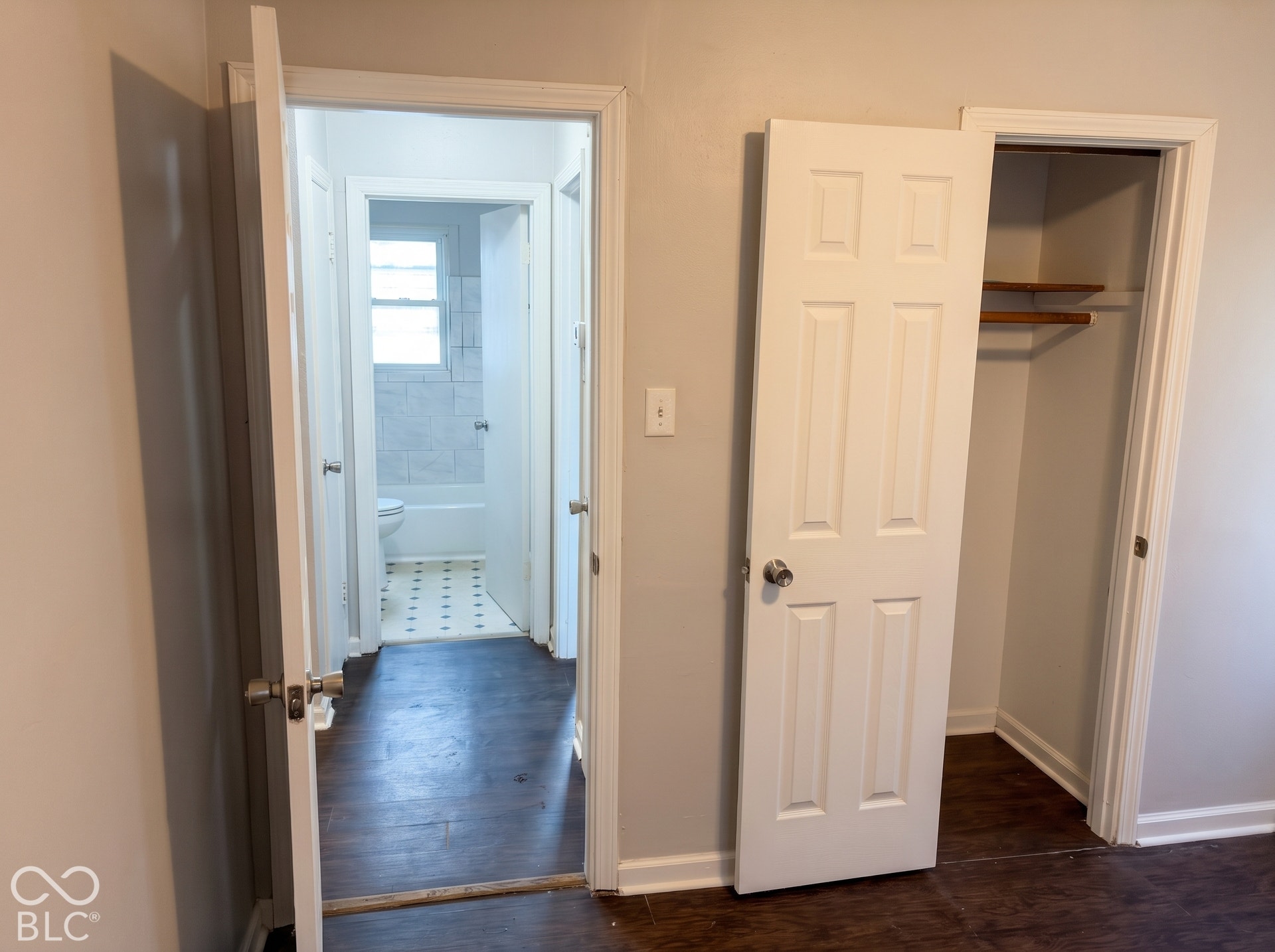 Wood-finish flooring throughout, white paneled doors, and a built-in closet with shelving and hanging rod