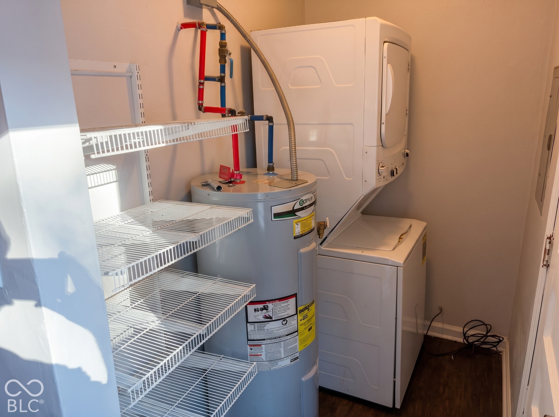 Utility closet featuring a water heater, stacked washer and dryer, and wire shelving