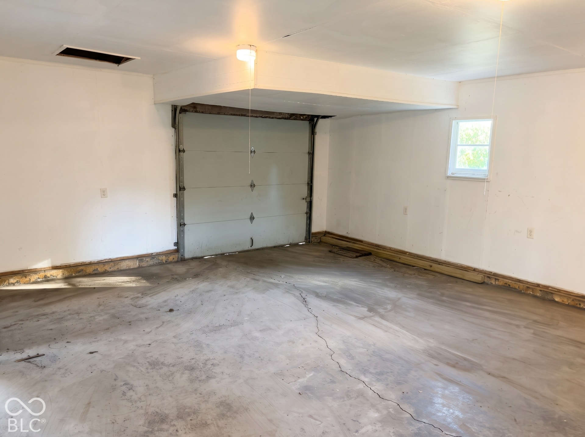 Garage space with a single overhead door, concrete flooring, and an elevated window