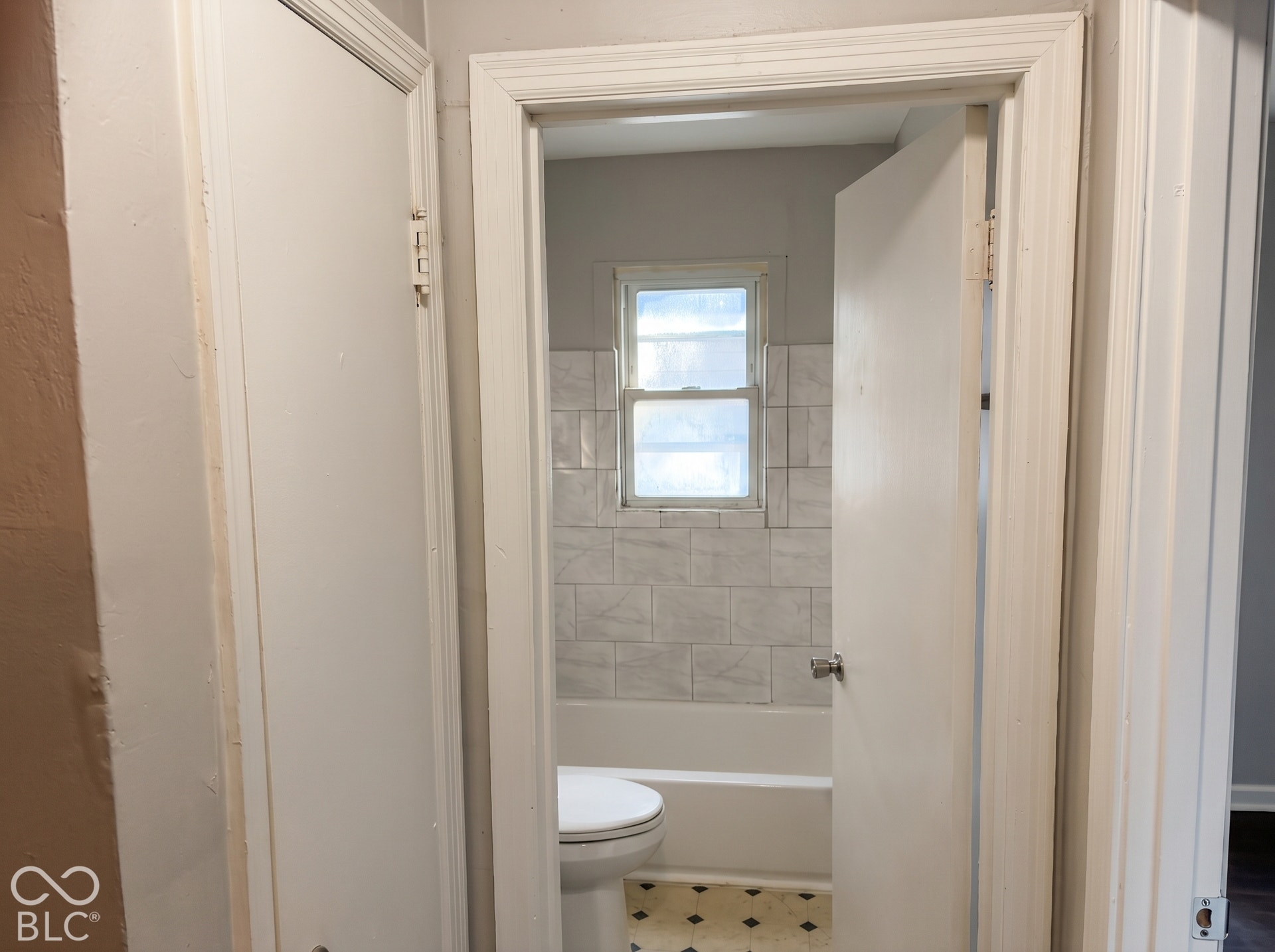Bathroom featuring a window, white subway-style wall tiling, and a white bathtub