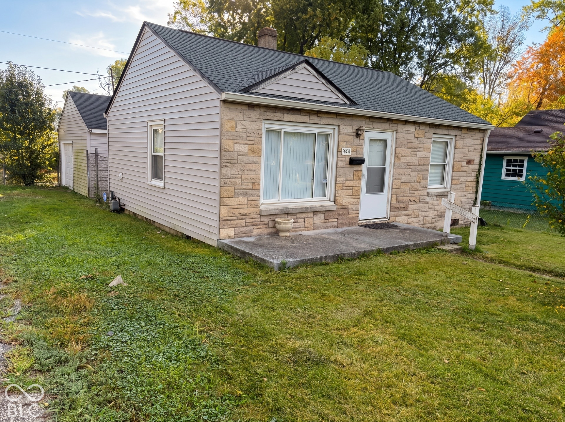 Exterior featuring stone and siding finishes, a shingled roof, a paved front stoop, and a detached structure