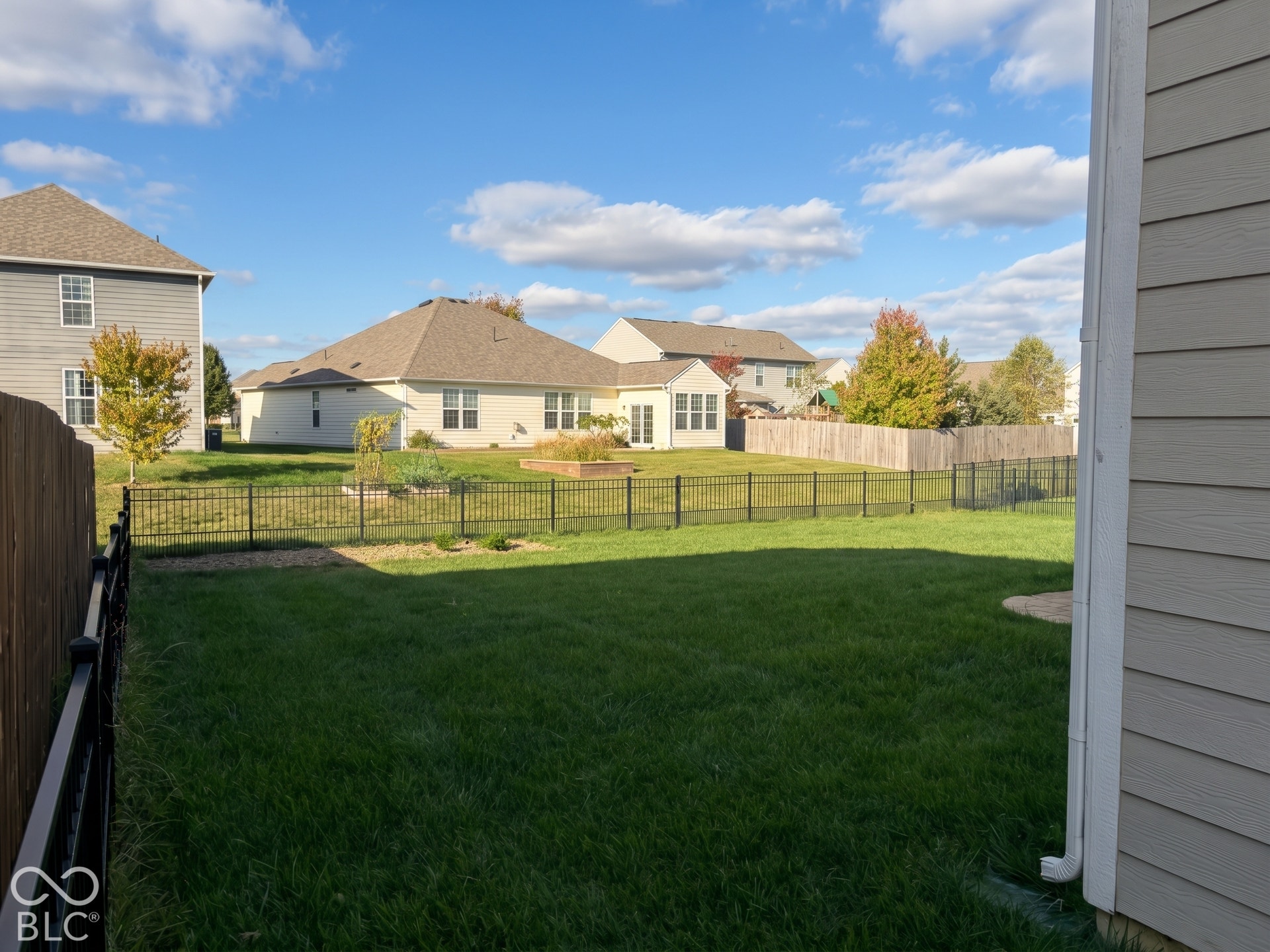 Virtually Altered - Expansive lawn area with a black metal fence and garden bed