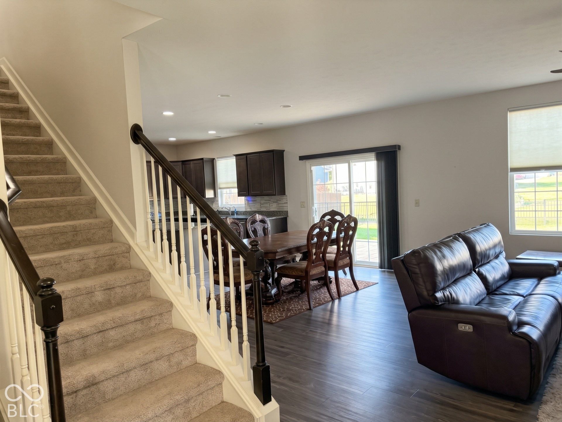 Virtually Altered - Open-concept living area with dark wood-finish flooring, a sliding glass door, and recessed lighting