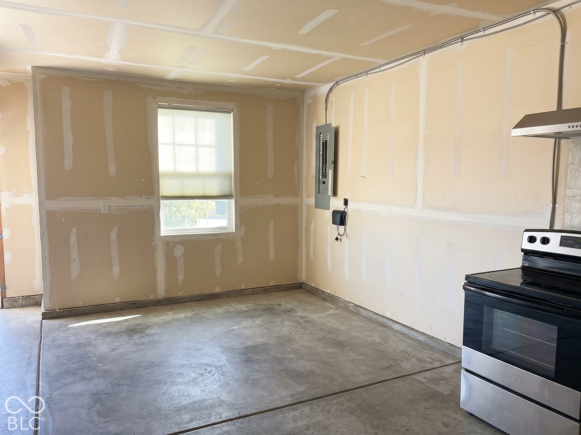 Virtually Altered - Unfinished interior space with an exposed electrical panel, a window with a roller shade, and a range with a stainless steel oven