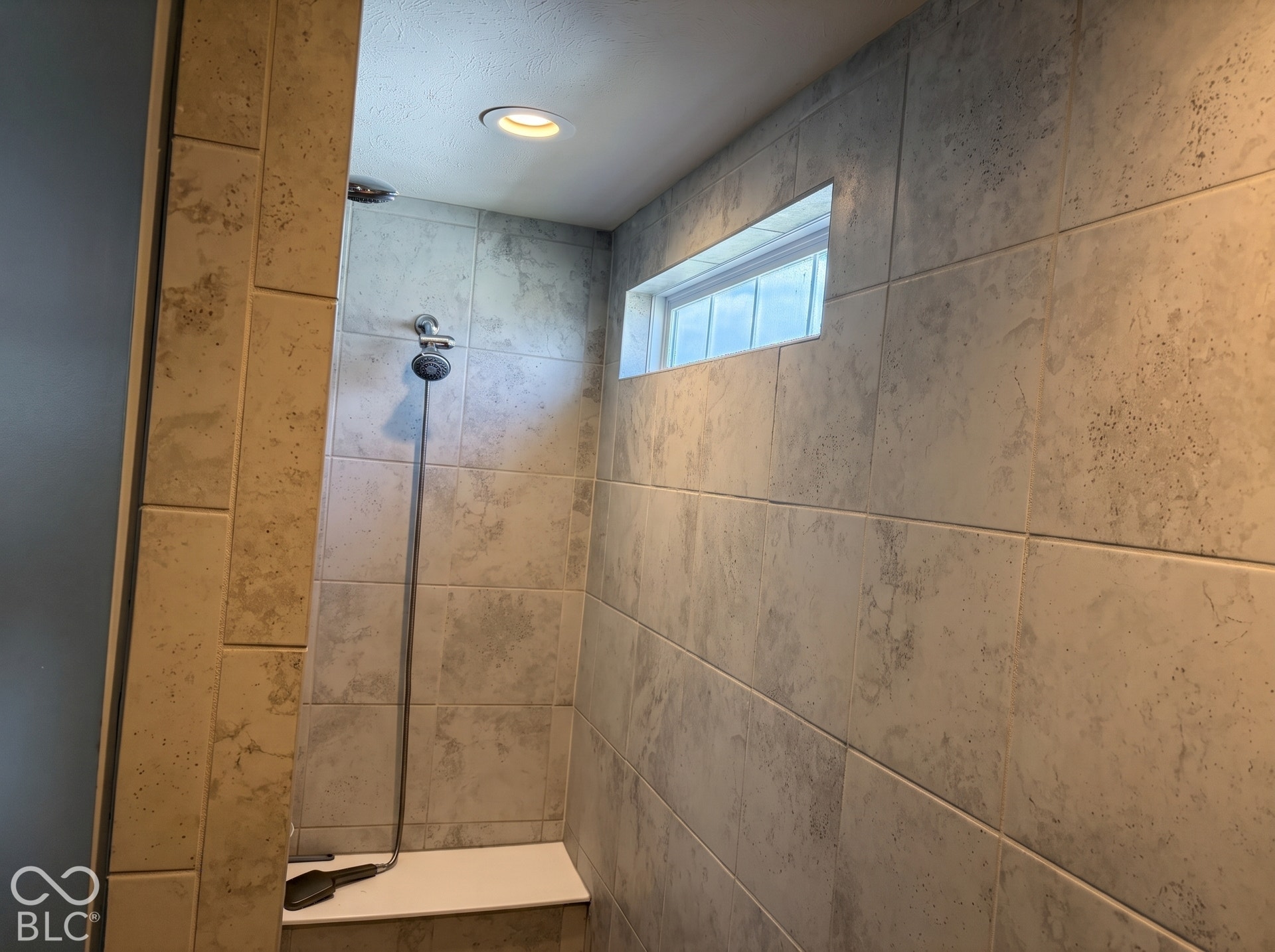 Virtually Altered - Master bathroom with tiled shower with a built-in bench, recessed lighting, and a transom window