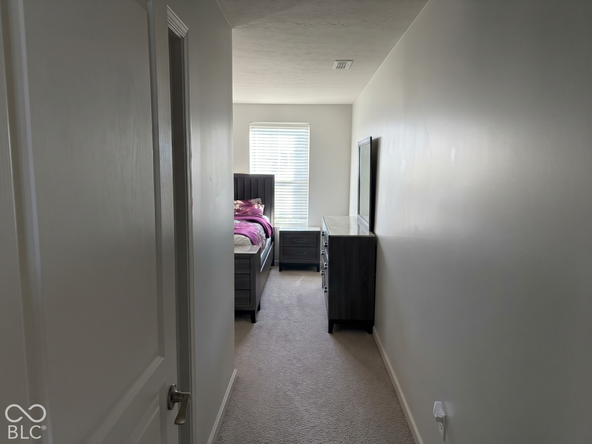 Virtually Altered - Entrance to Bedroom 2 with carpeted hallway with light-toned walls leading to a room with a window and horizontal blinds