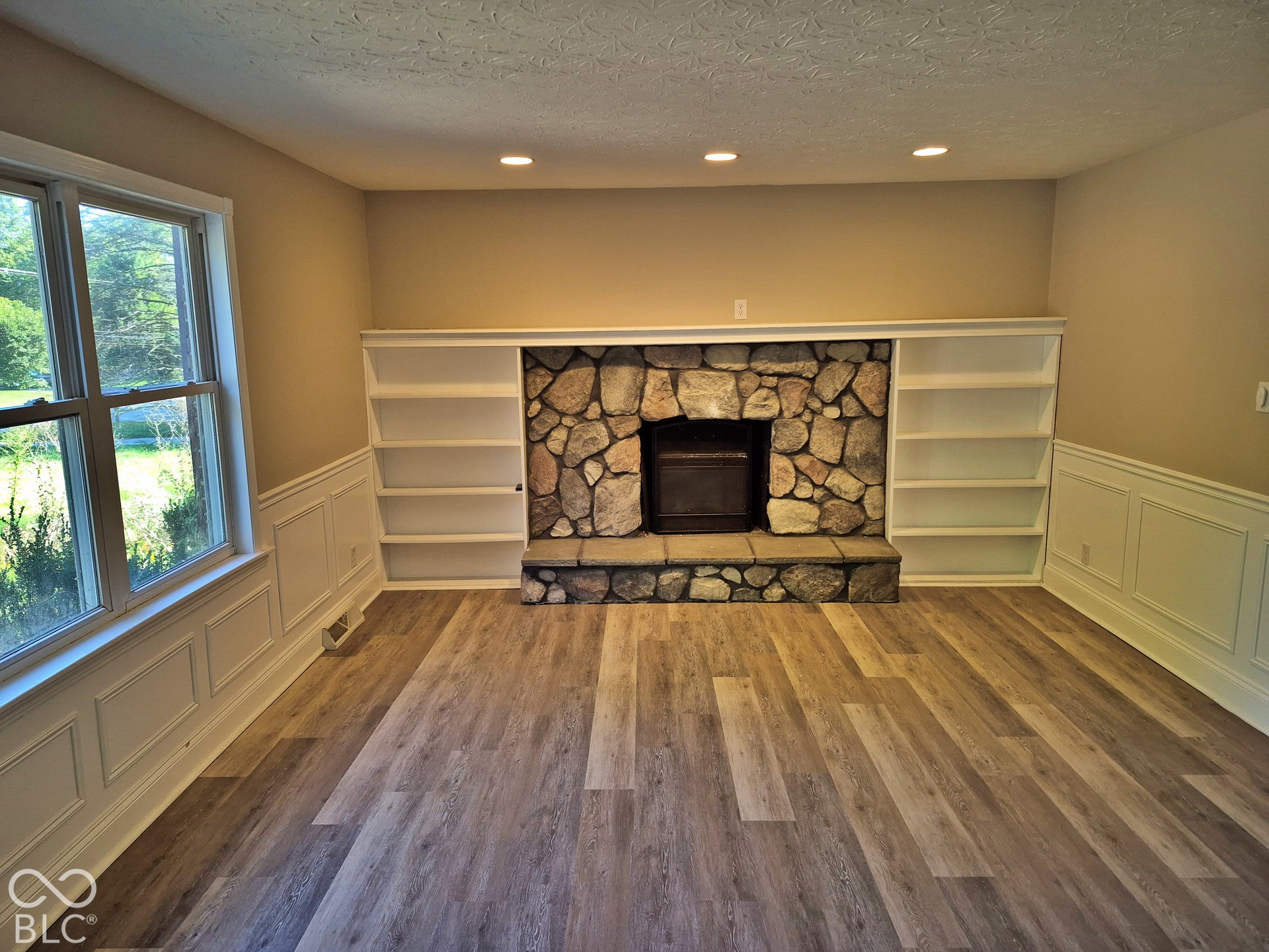 Stone-clad fireplace with hearth, built-in shelving, wood-finish flooring, wainscoting, and recessed lighting