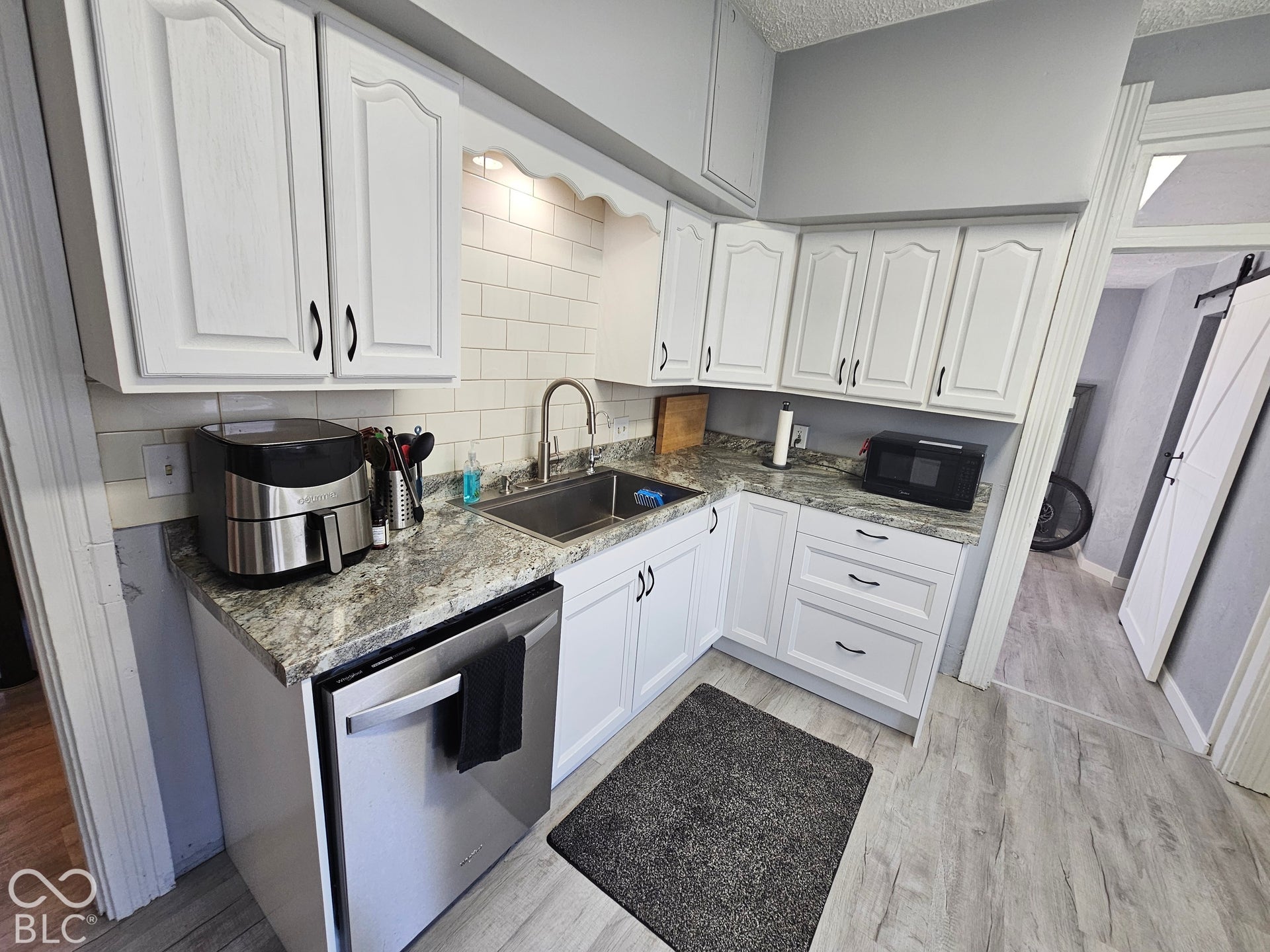917 W 8th Street, Anderson, IN 46016 White cabinetry with black hardware, subway tile backsplash, stainless steel sink, wood-finish flooring, and a stainless steel dishwasher
