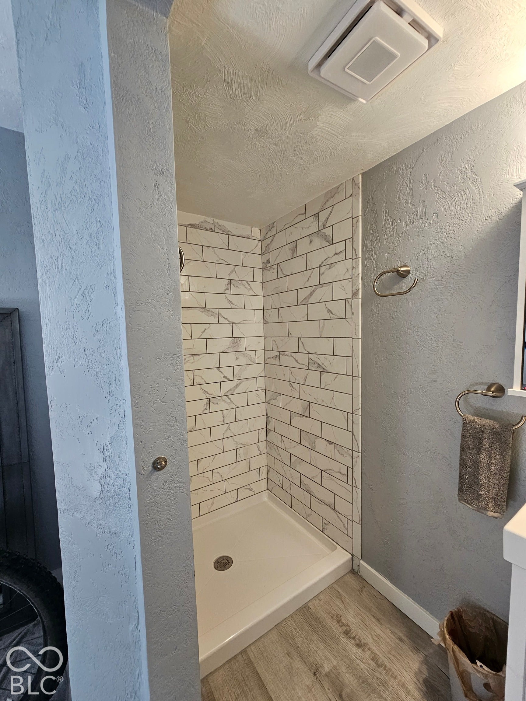 917 W 8th Street, Anderson, IN 46016 Shower stall with white subway-style tile, white shower pan, wood-finish flooring, and a ceiling-mounted ventilation fan