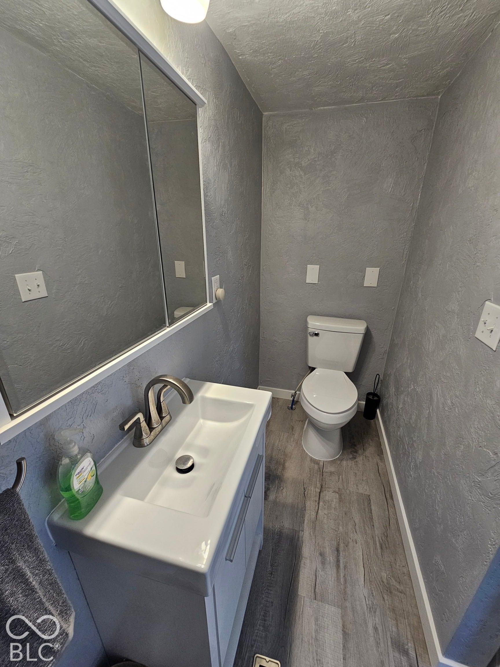 917 W 8th Street, Anderson, IN 46016 Vanity with integrated sink, wood-finish flooring, wall-mounted mirror with integrated lighting, and a commode