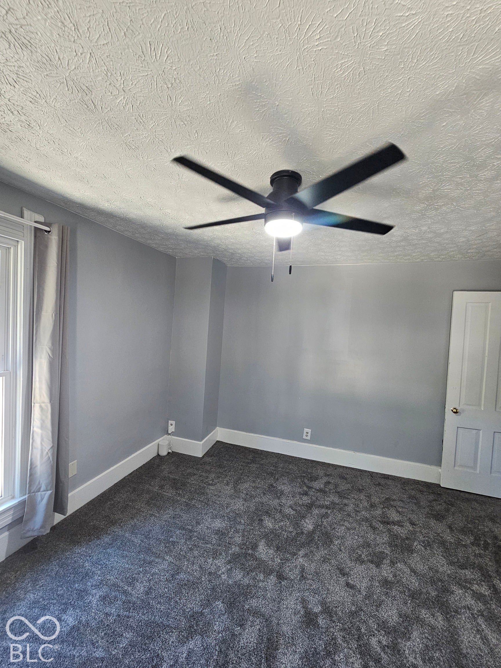 917 W 8th Street, Anderson, IN 46016 Gray wall paint, textured ceiling, black ceiling fan with integrated lighting, gray carpet, and white trim