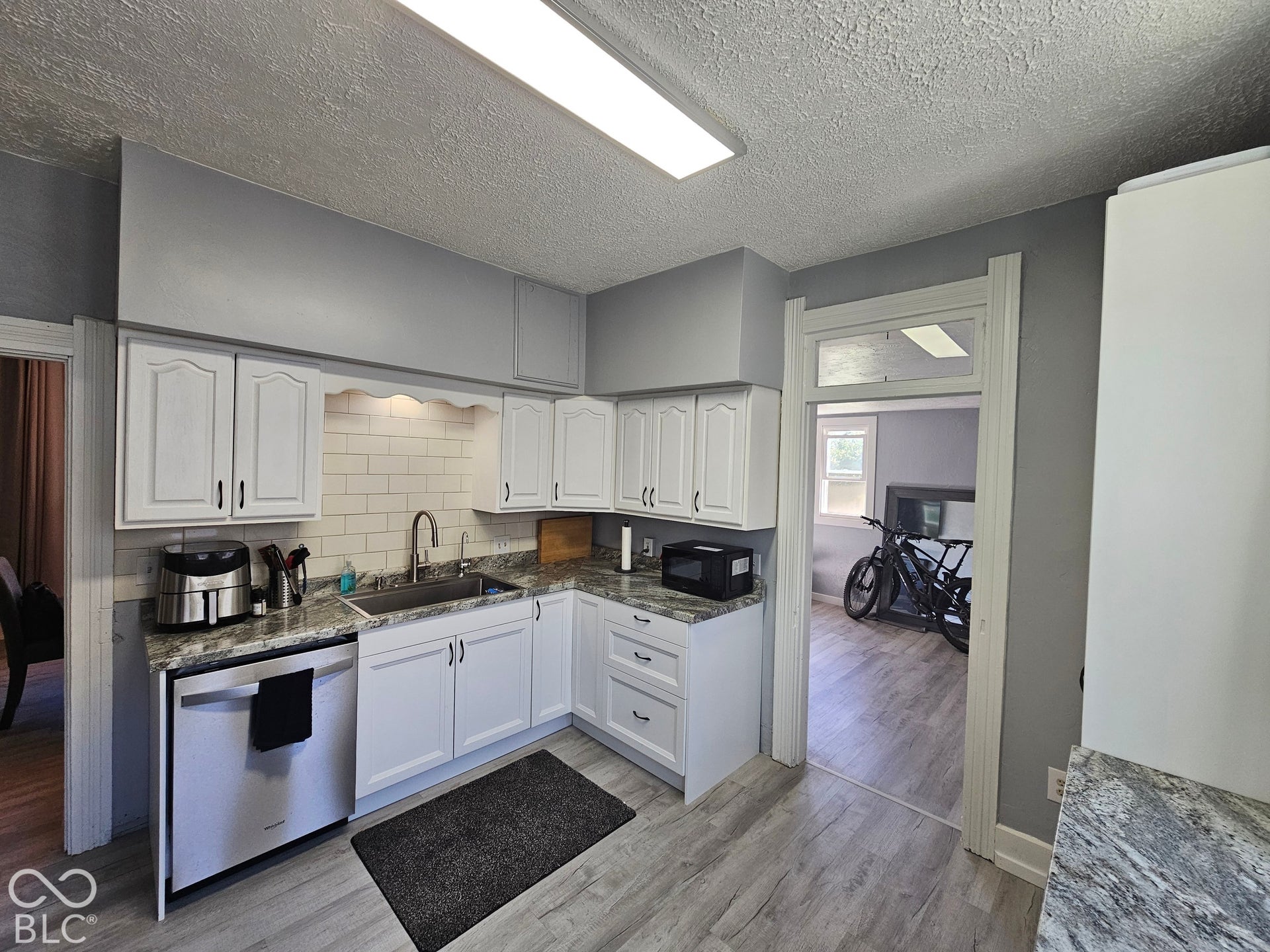 917 W 8th Street, Anderson, IN 46016 White cabinetry with black hardware, subway tile backsplash, stainless steel sink, wood-finish flooring, and light-toned countertops