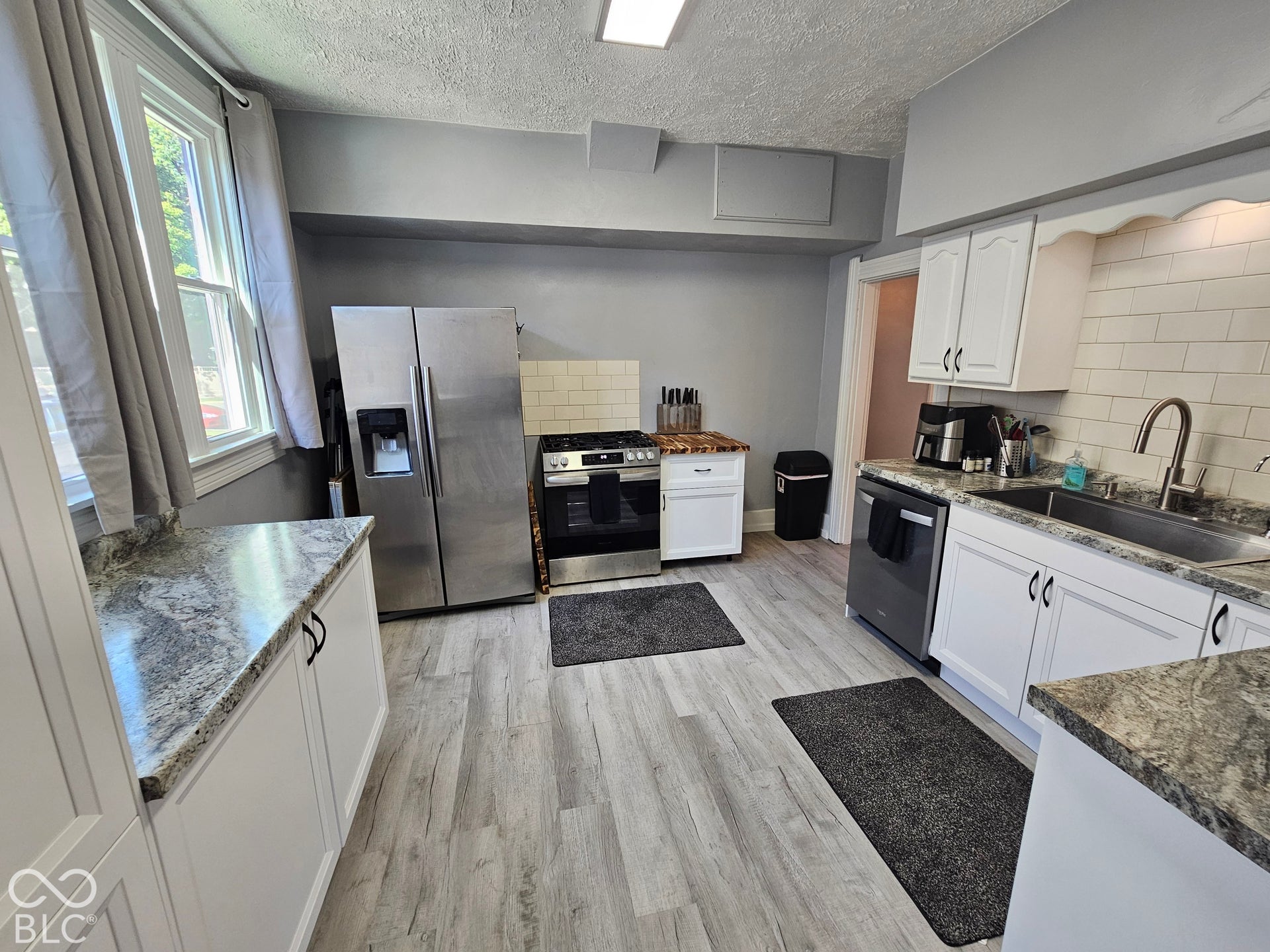 917 W 8th Street, Anderson, IN 46016 Kitchen featuring light wood-finish flooring, white cabinetry with black hardware, and speckled countertops