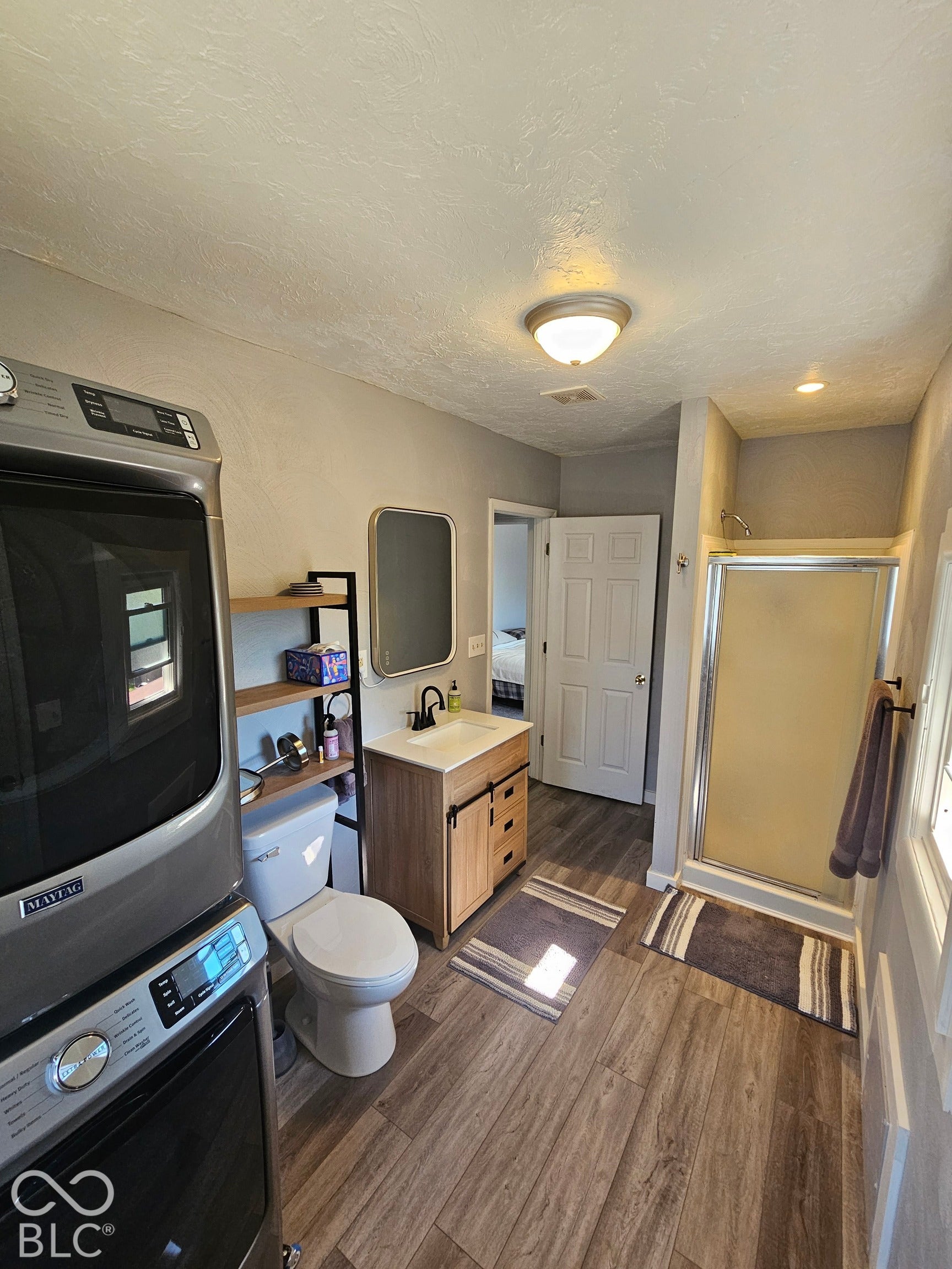 917 W 8th Street, Anderson, IN 46016 Wood-finish flooring, single vanity with wood-finish cabinetry, black faucet, rectangular mirror, and a shower enclosure