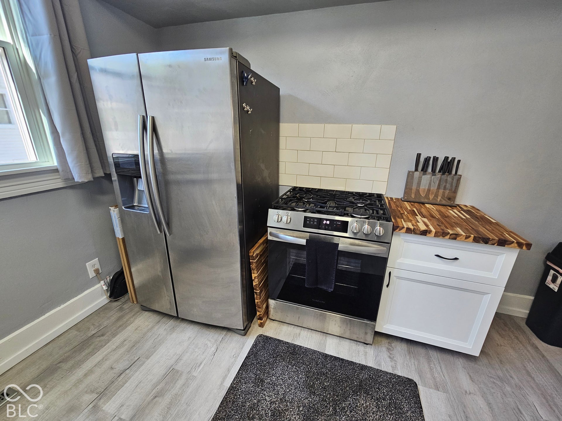 917 W 8th Street, Anderson, IN 46016 Stainless steel side-by-side refrigerator, stainless steel gas range, butcher block countertop, white shaker-style cabinetry, and wood-finish flooring