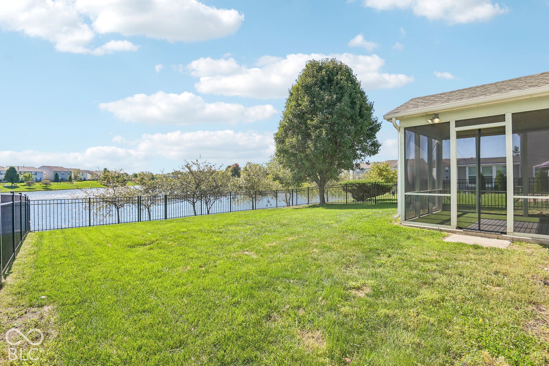 Expansive lawn area, screened porch, fenced perimeter, mature tree, and water frontage
