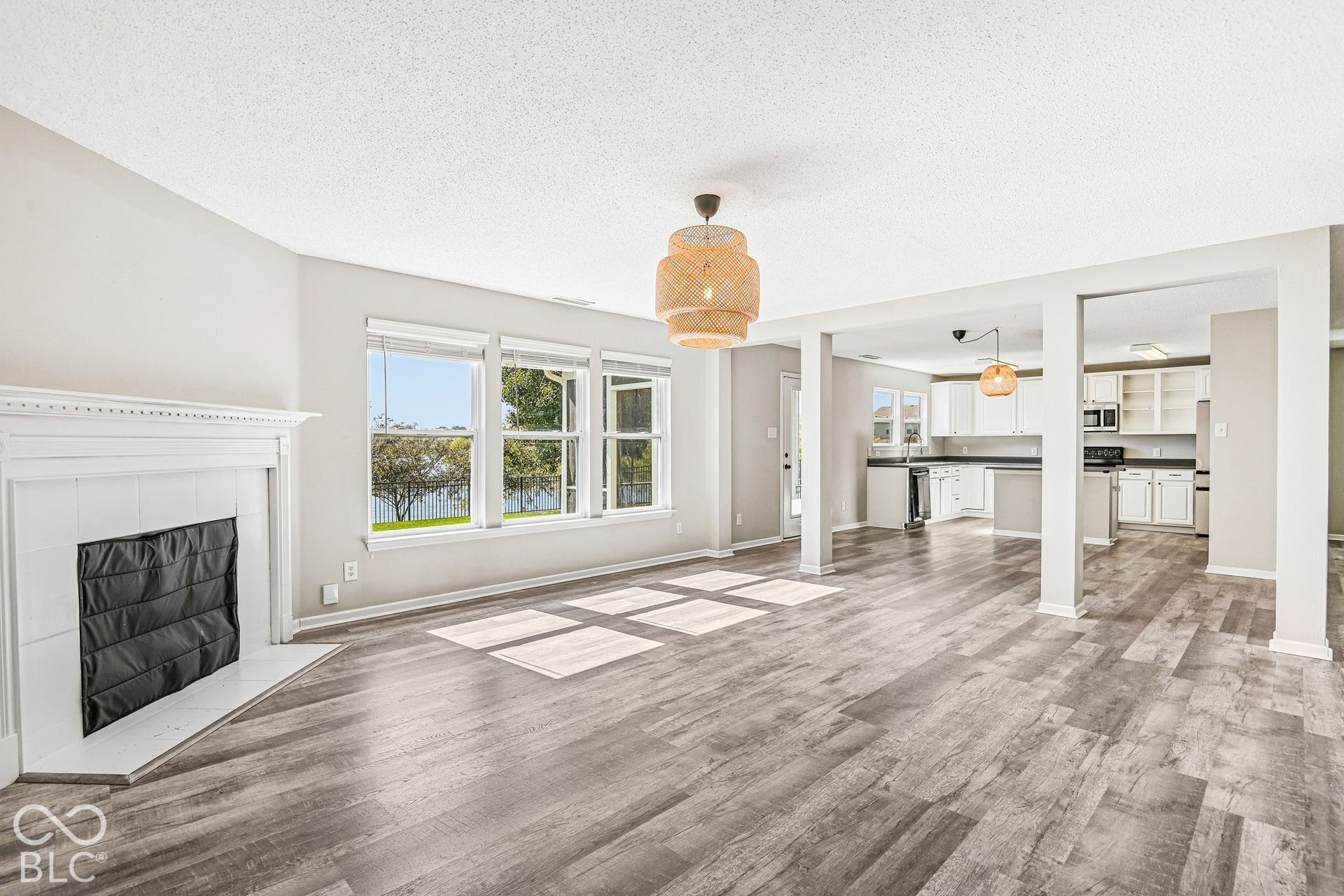 Open-concept living space featuring wood-finish flooring, a white fireplace, and a kitchen with white cabinetry and dark countertops