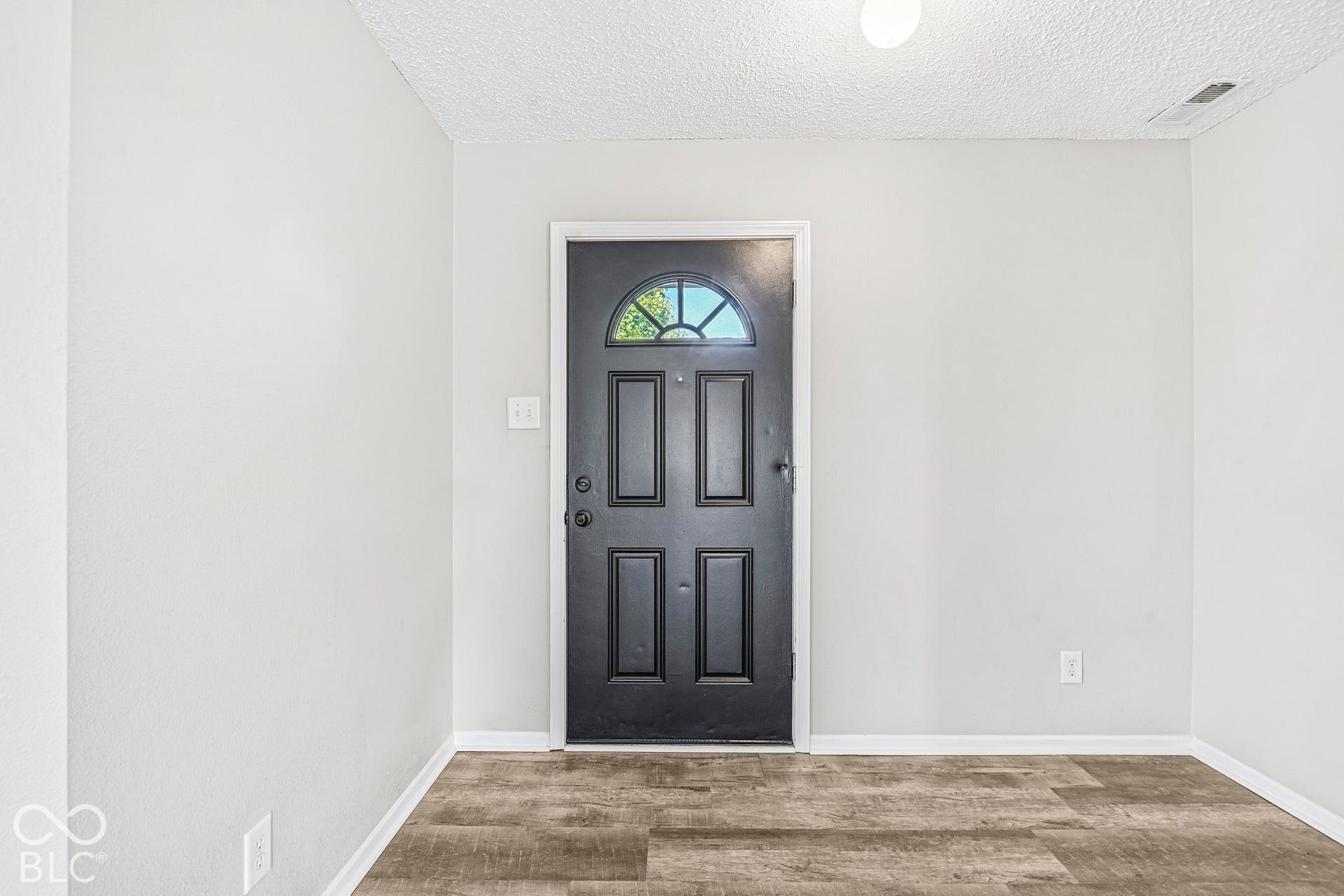 Entry door with an arched transom window, wood-finish flooring, and light-toned walls