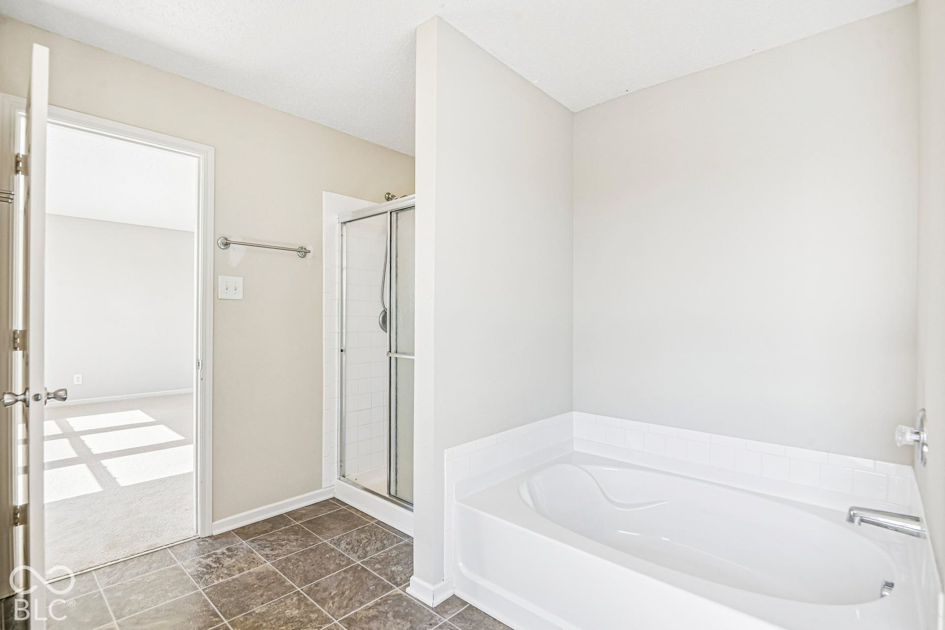 Full-size bathtub with white tile surround, adjacent shower with glass enclosure, and dark-toned floor tiling