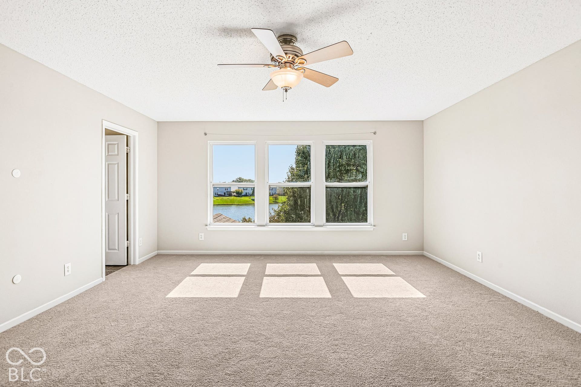 Carpeted room featuring a ceiling fan with light, multiple windows, and a water body visible beyond the property