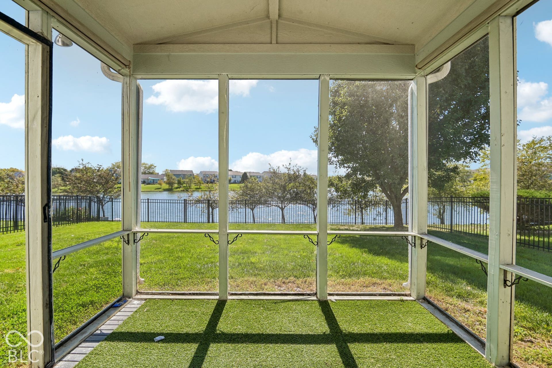 Screened porch with artificial turf flooring, offering expansive water scenery and a black metal fence