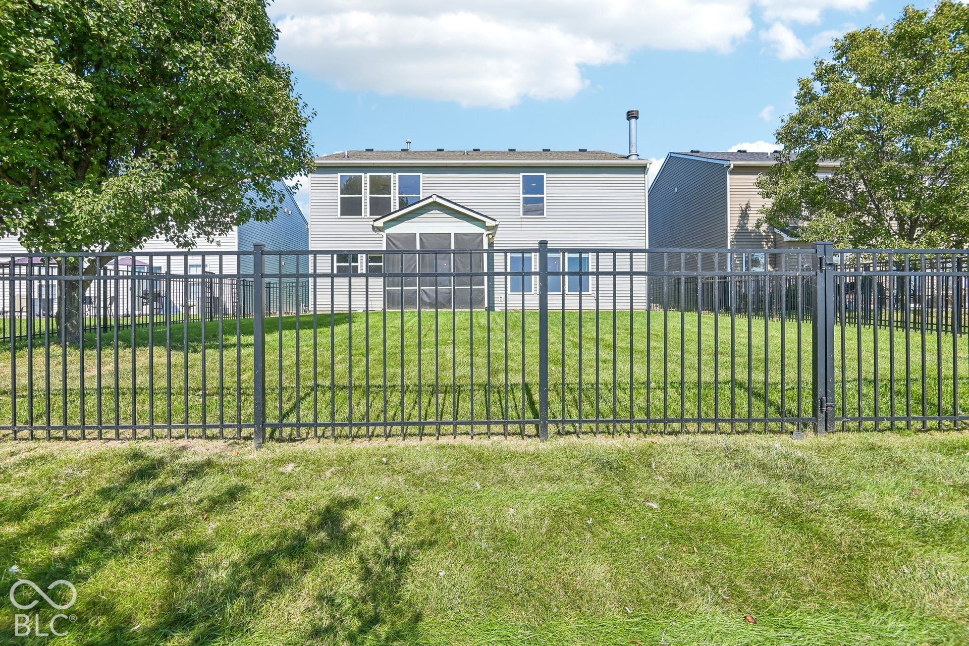 Manicured lawn with a black metal fence, screened-in porch, and a light-colored siding exterior