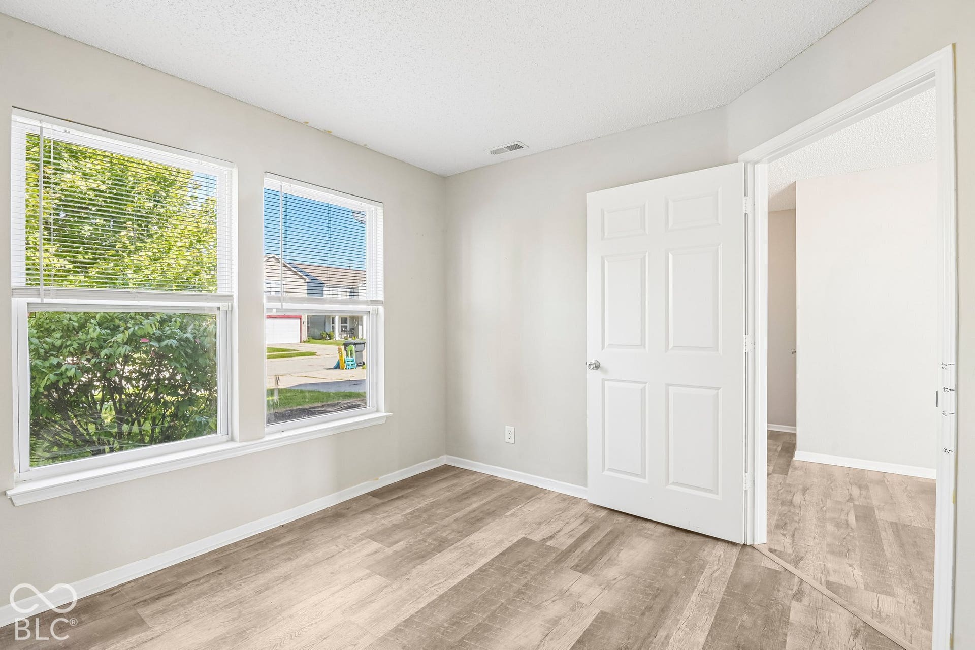 Wood-finish flooring, two window openings, textured ceiling, and a paneled door with a chrome knob