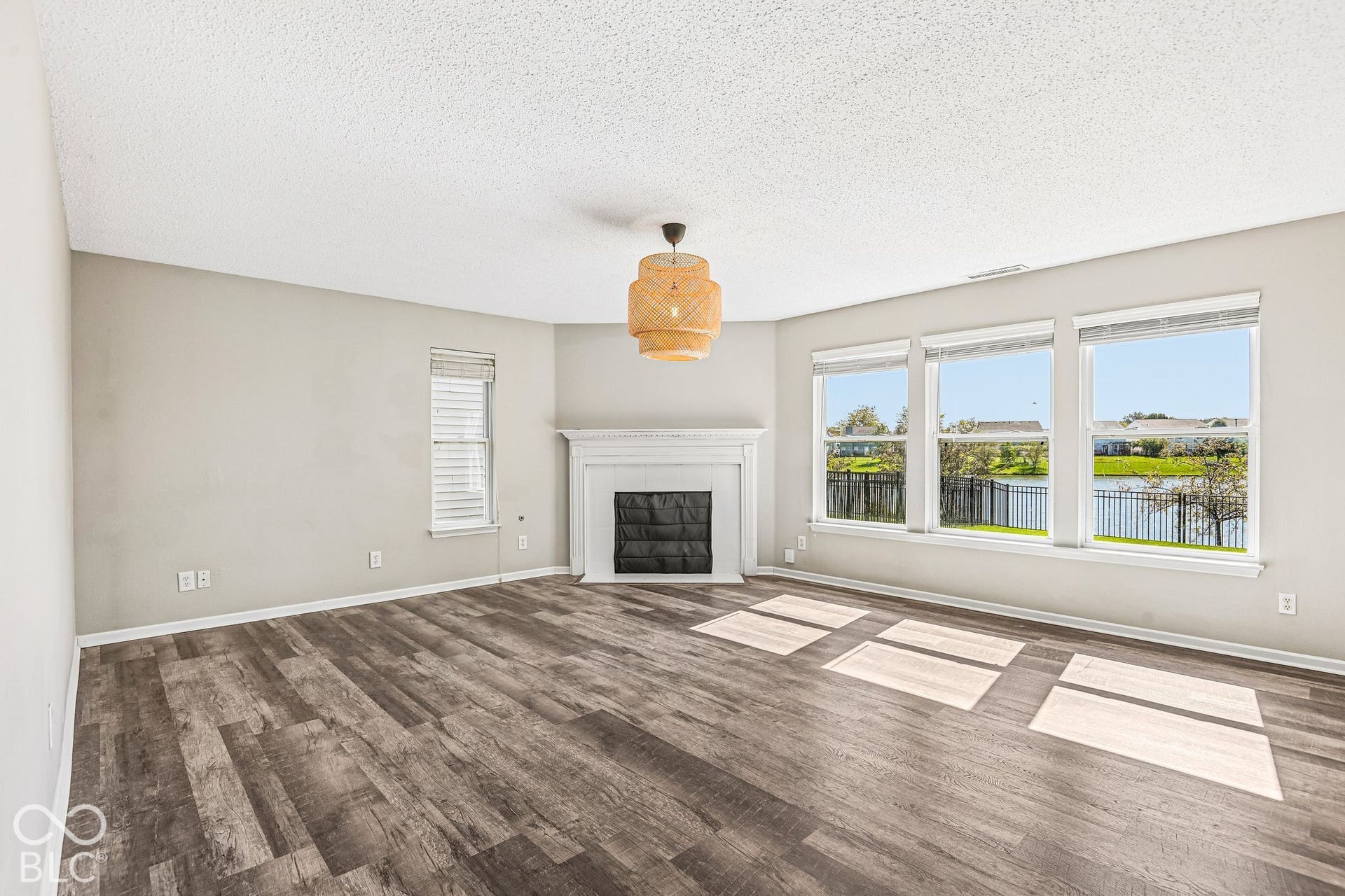 Spacious room with wood-finish flooring, a white mantel fireplace, and a large window array