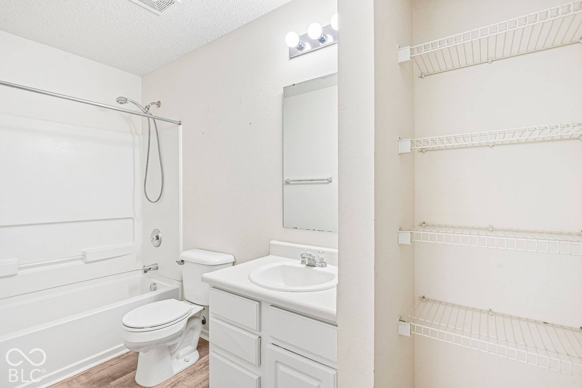 Bathroom featuring a built-in bathtub with shower, single vanity with integrated sink, wood-finish flooring, and wire shelving