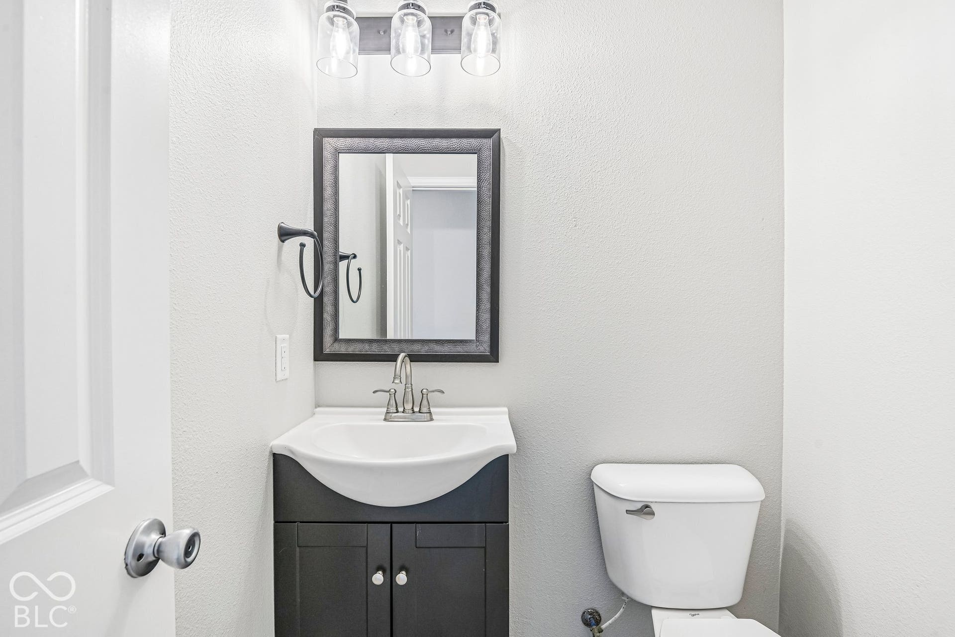 Vanity with an integrated white sink, dual-door cabinet, framed mirror, and a three-light fixture