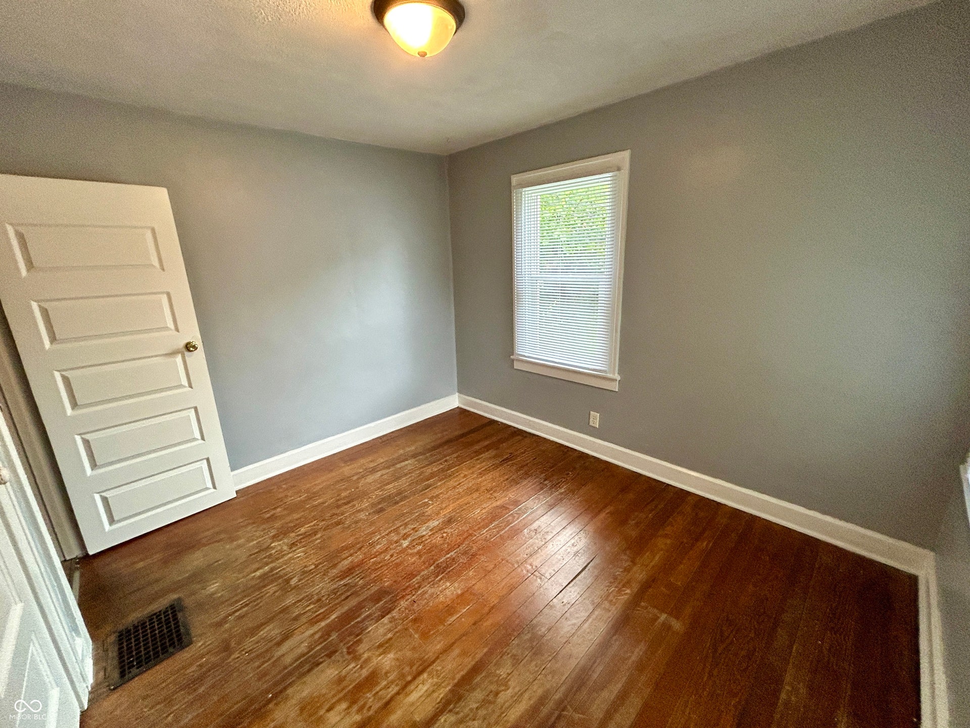 Bedroom featuring wood-finish flooring, a single window with blinds, and light gray wall paint