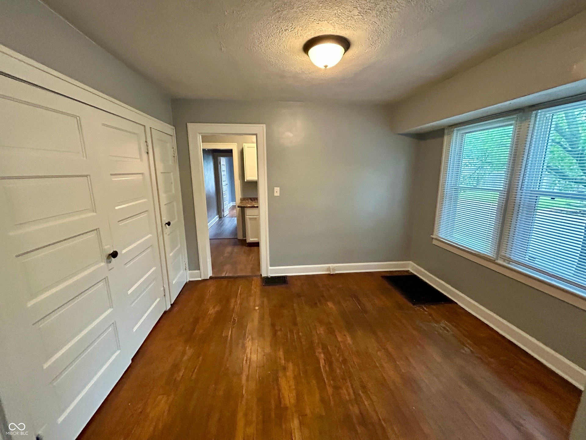 Room featuring wood-finish flooring, two window openings with blinds, and white trim