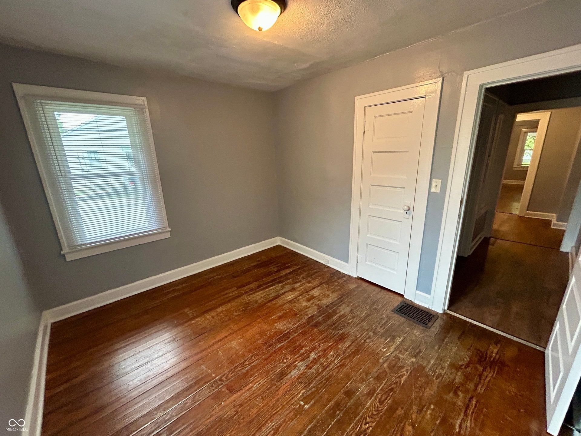 Room featuring wood-finish flooring, light gray walls, white trim, and a white paneled door