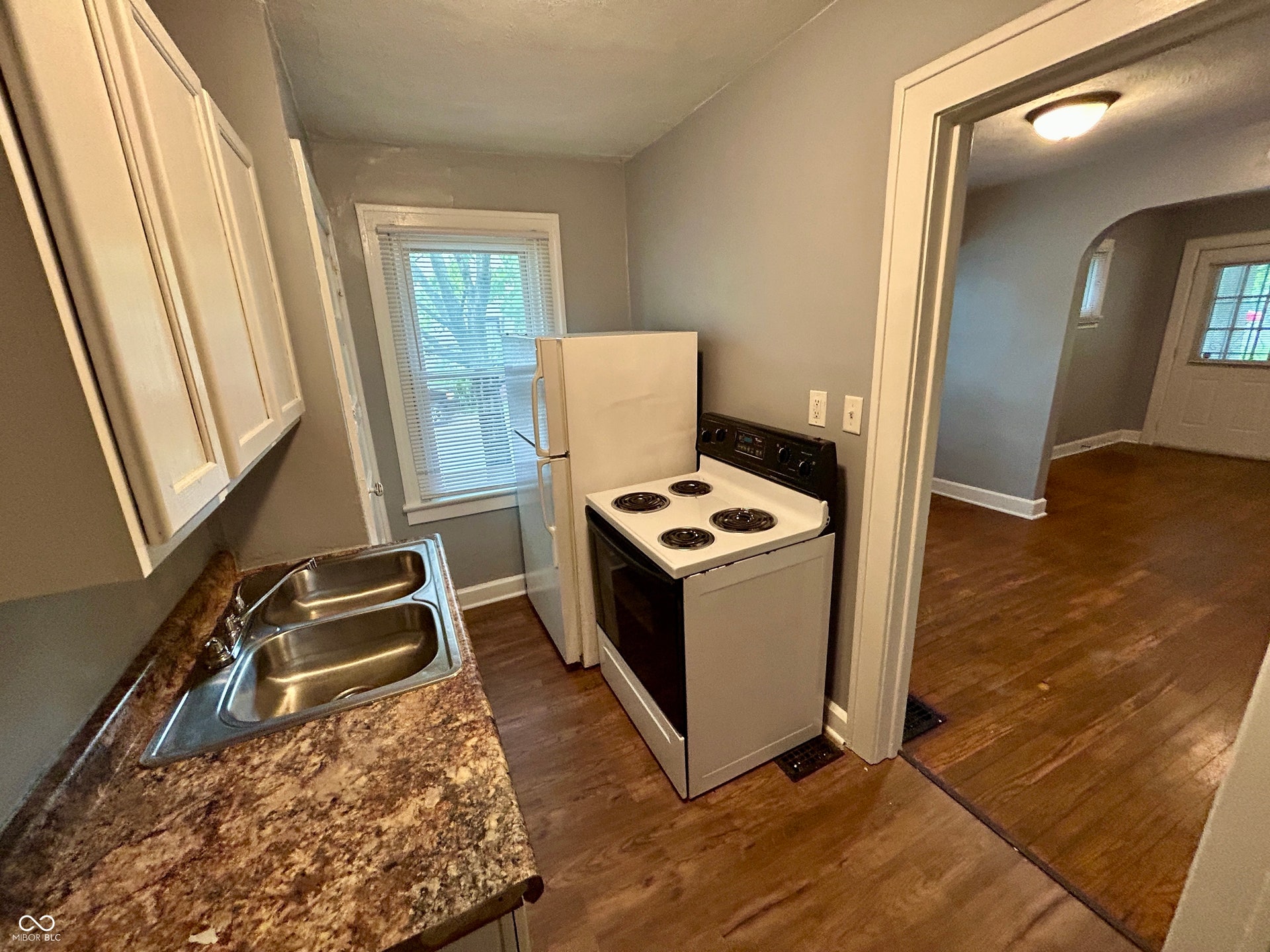 Kitchen featuring wood-finish flooring, a double basin stainless steel sink, patterned countertop, and white cabinetry