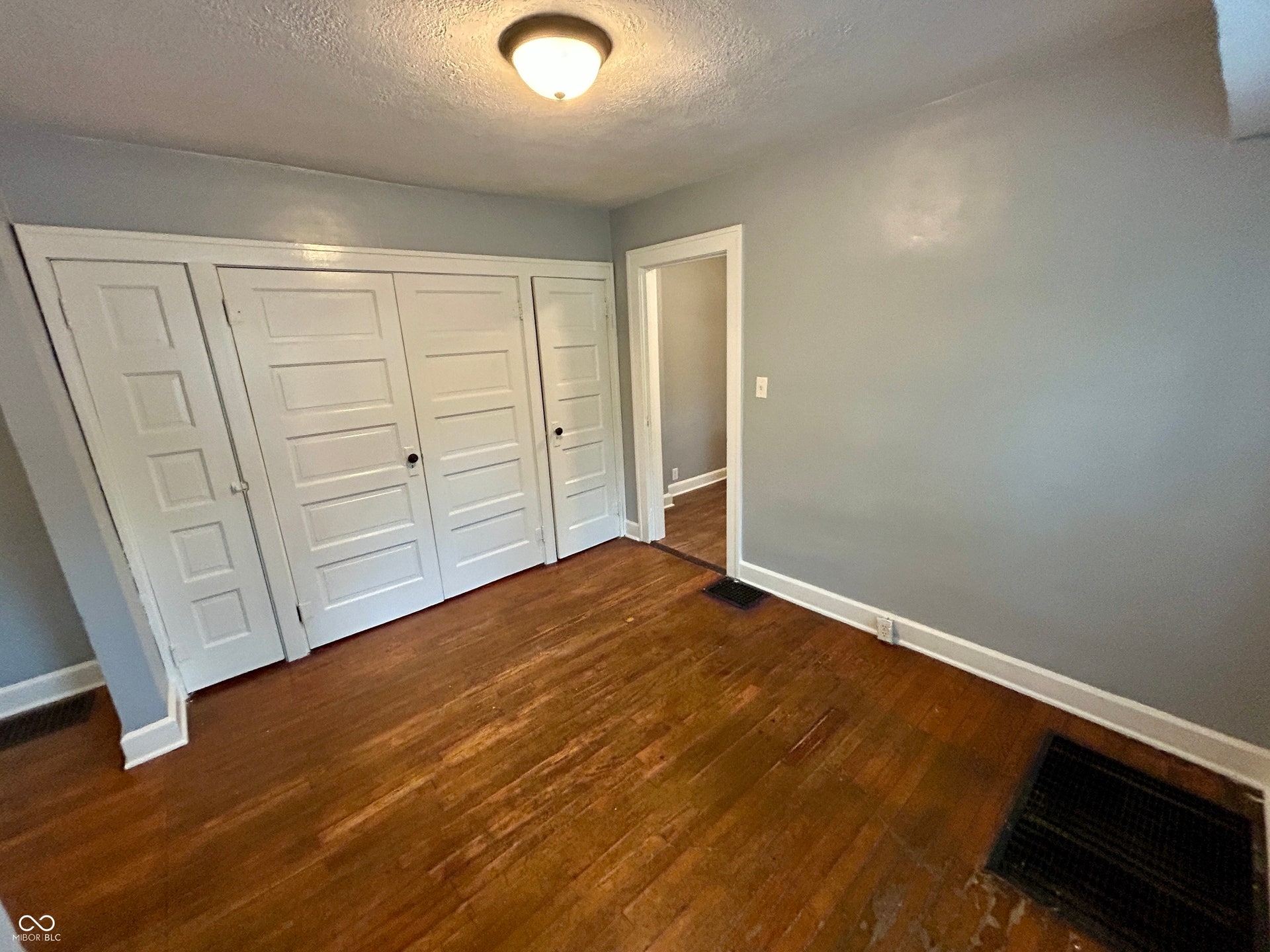 Bedroom featuring wood-finish flooring, light gray wall paint, and extensive built-in closet storage with paneled doors