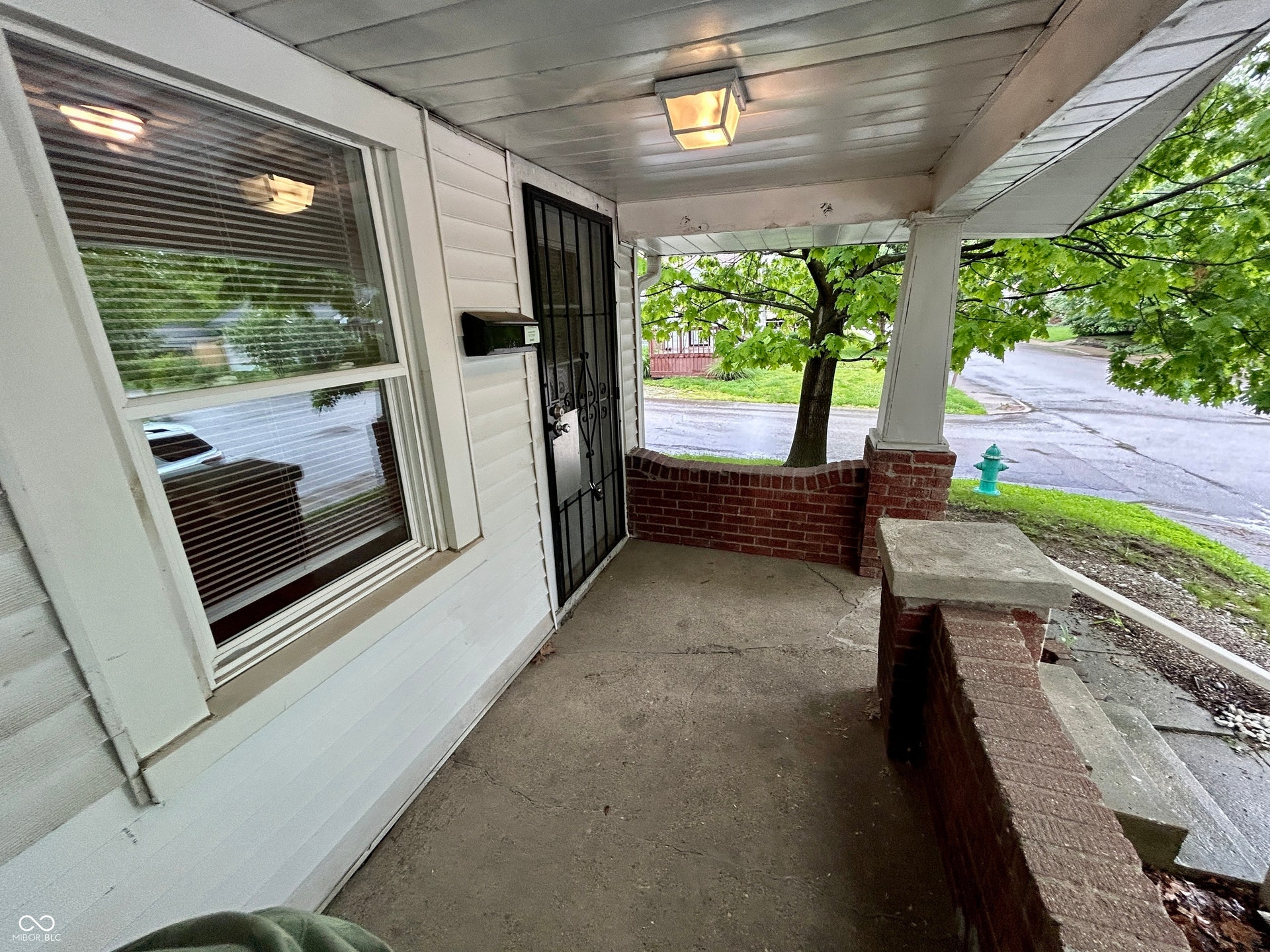 Covered concrete front porch featuring a security door, white vinyl siding, and brick knee wall with a concrete cap