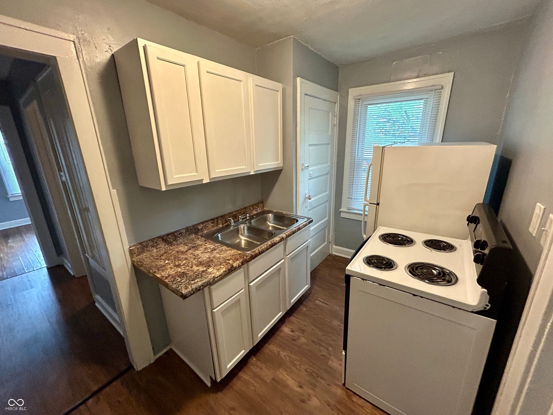 Kitchen featuring wood-finish flooring, light grey walls, white cabinetry, a double basin stainless steel sink, and a patterned countertop