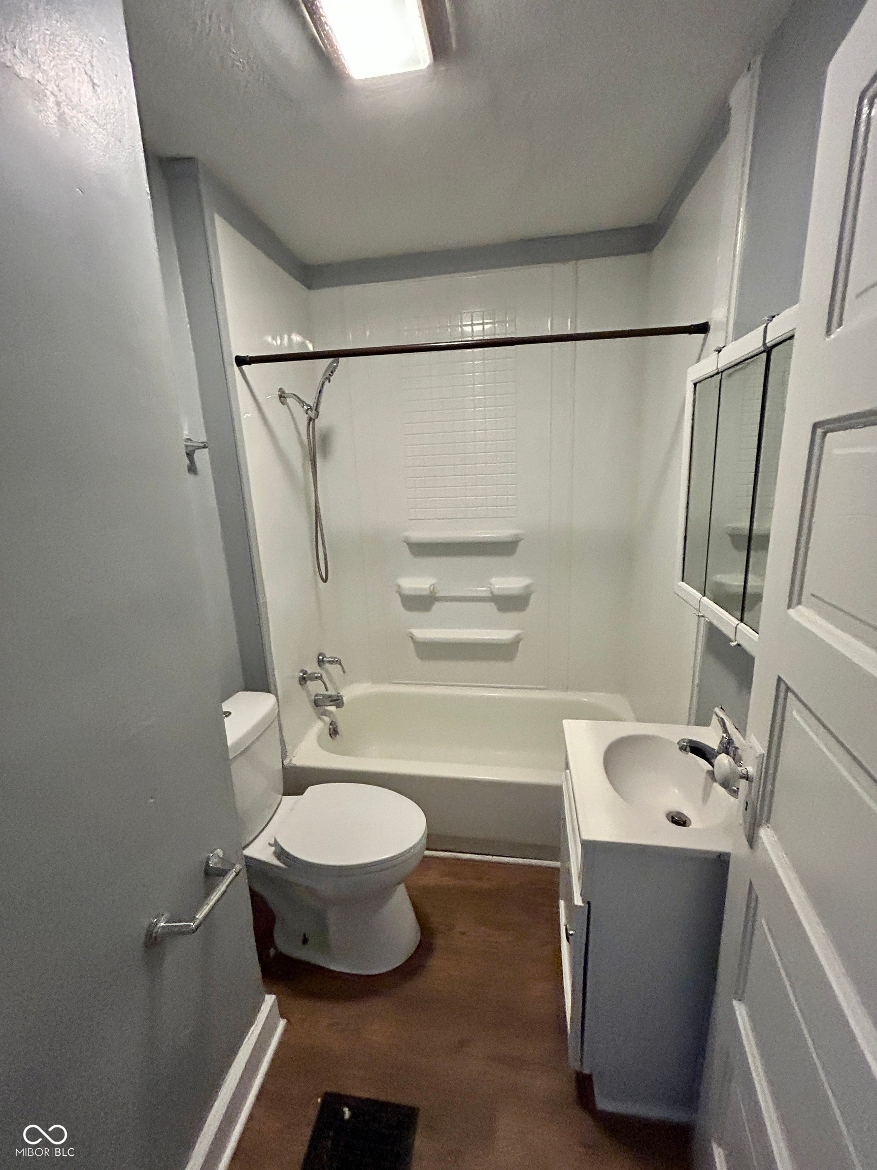 Full bathroom featuring a white tub/shower combination with tile surround, white vanity with integrated sink, wood-finish flooring, and a mirrored medicine cabinet