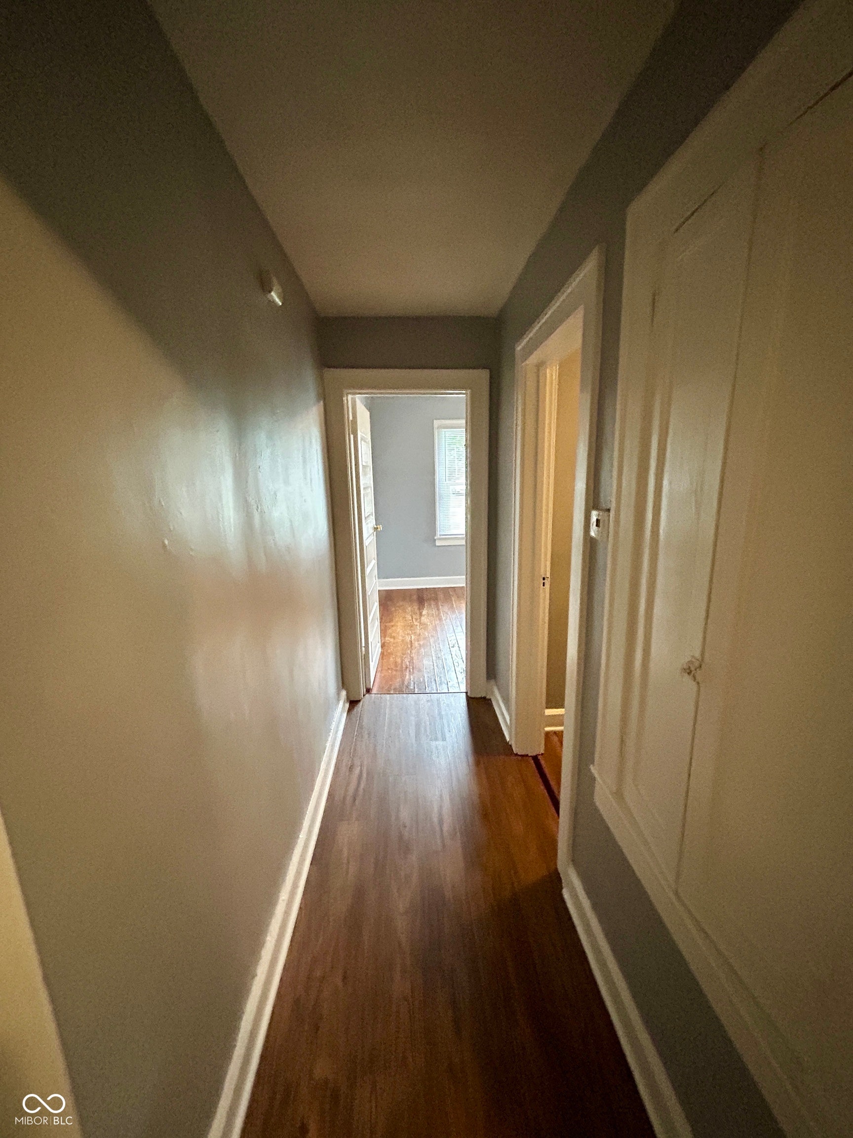 Hallway with dark wood-finish flooring, light grey painted walls, white baseboards, and white trim around doorways