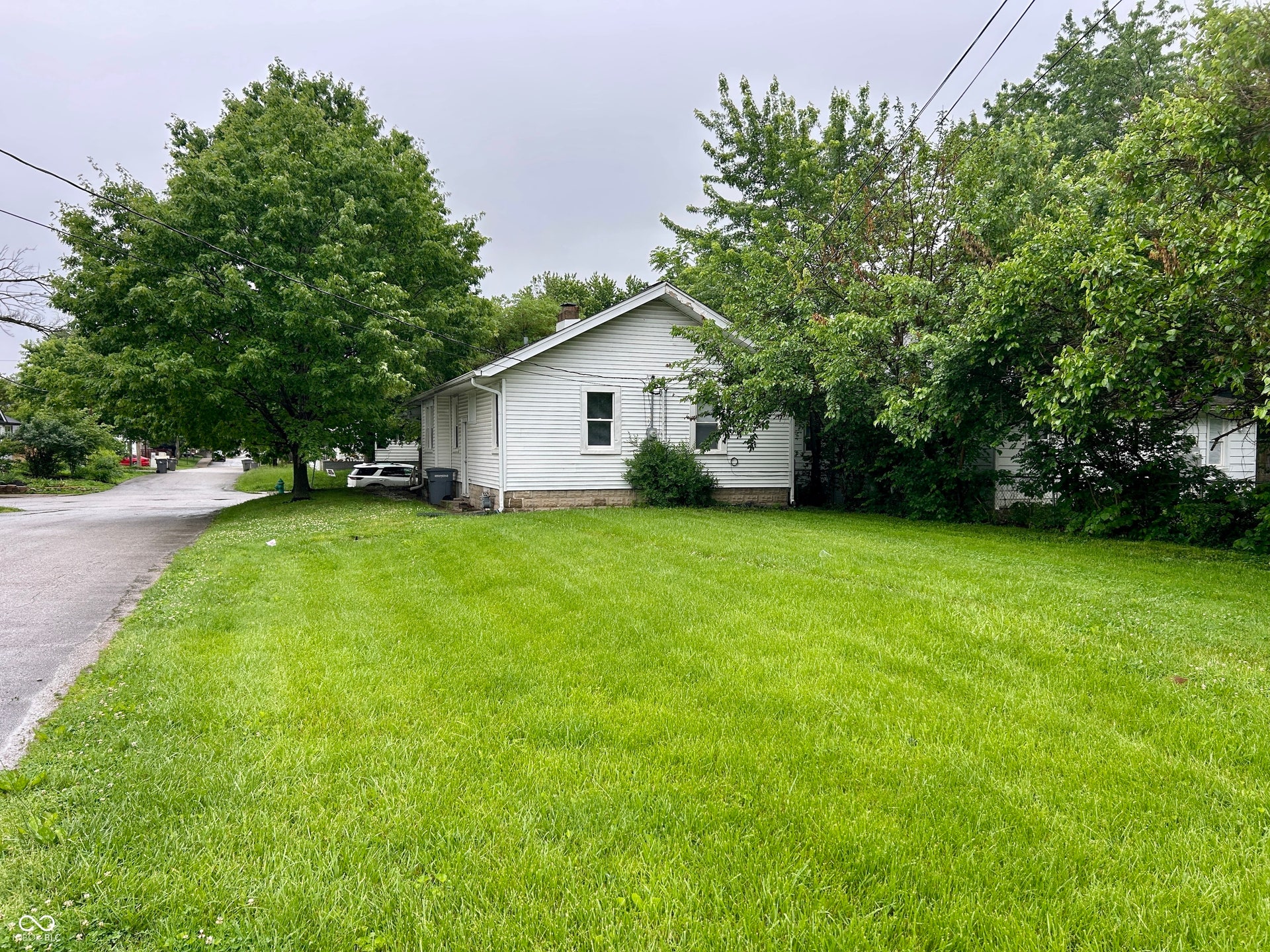 White siding exterior with a prominent large tree, expansive green lawn, and additional mature trees