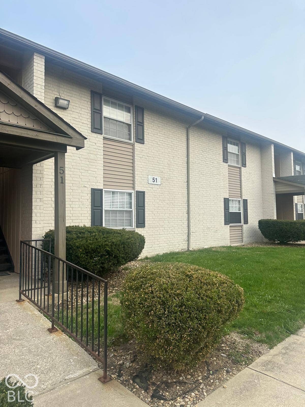 Brick and siding exterior with dark shutters, featuring a covered entryway with a metal handrail