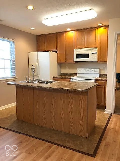 Kitchen featuring wood-finish cabinetry, a central island with a sink, white appliances, and recessed lighting