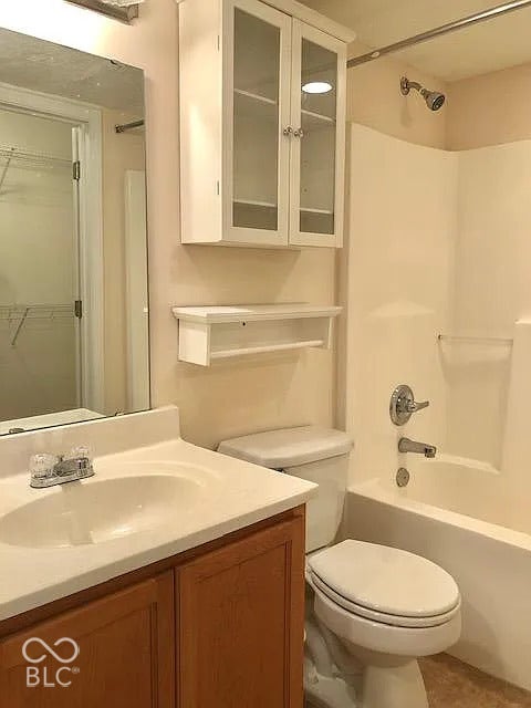 Bathroom featuring a wood-finish vanity with an integrated sink, a full-width mirror, a wall-mounted cabinet with glass-front doors, a built-in shelf with a towel bar, and a shower-over-tub combination with chrome fixtures