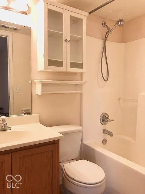 Vanity with a single basin sink, white built-in storage cabinet, white over-toilet shelving, and a white bathtub with a shower attachment