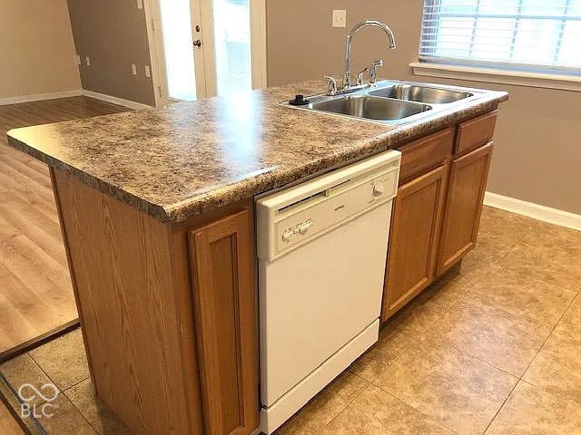 Kitchen island featuring a double basin stainless steel sink, gooseneck faucet, integrated dishwasher, and wood-finish cabinetry